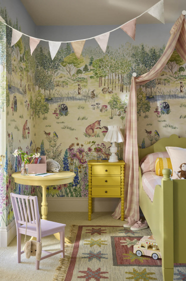 Children's bedroom featuring pastel mural wallpaper (Potter's Woodland - Spring) with a bed to the right and table and chair to the left with bunting hanging on the ceiling.