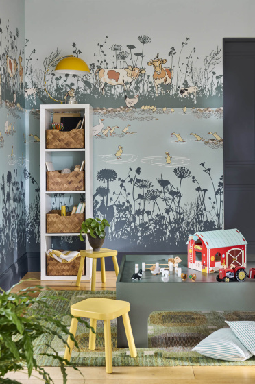 Children's playroom featuring blue mural wallpaper (Riverside Capers - Moo) with storage space to the left alongside yellow stools and toys in the foreground.