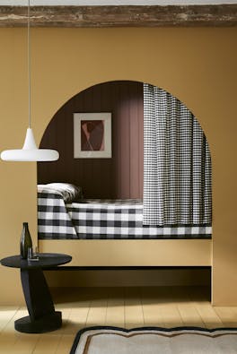 Bedroom with yellow painted arch (Bassoon) leading to a gingham bed with curtain.