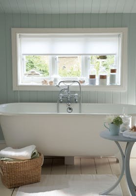 Paneled bathroom painted in light green (Salix) with a white bathtub under a large window.