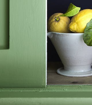 Close-up of deep green kitchen cupboards painted in 'Garden', and partly open revealing two lemons and glassware inside.