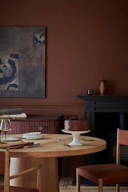 Dining space colour drenched in deep brown shade 'Ganache' with a wooden table and chairs under abstract wall art.