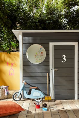 Dark grey (Scree) shed with toys outside and a bright yellow (Yellow-Pink) wall to the left.