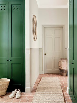 Hallway with dark green cupboard doors, neutral two-tone neutral walls and red brick flooring with a jute rug.