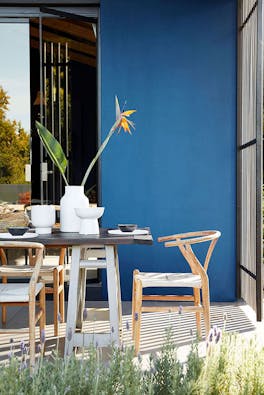 Outdoor breakfast patio space painted in rich blue 'Mazarine' with a wooden dining room table and chairs.