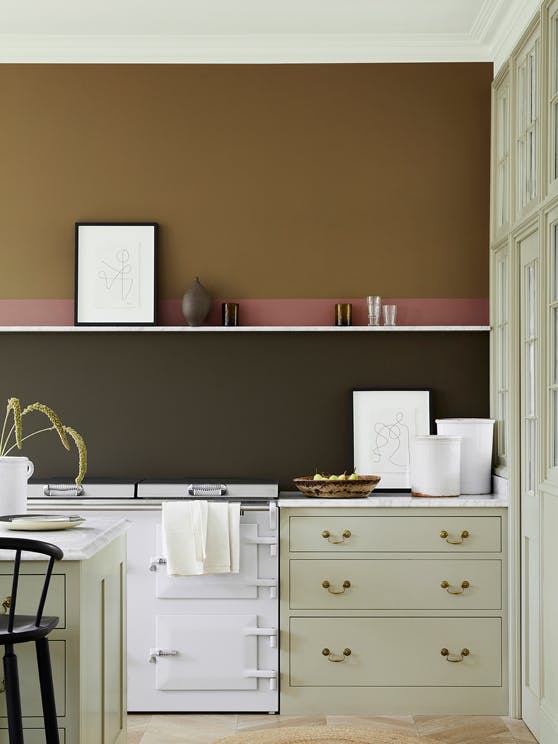 Kitchen with a bronze, red and deep stone wall, and cabinets painted in the neutral stone colour, 'Book Room Green'.