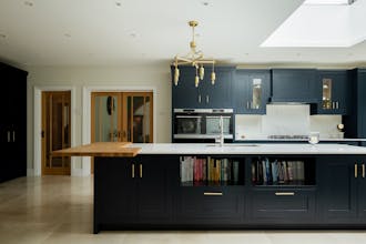 Ktchen featuring a large island with blue-black (Basalt) kitchen cupboards and a marble worktop, and lighting hanging above. 