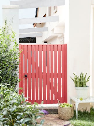 Statement Orange Aurora garden gate between neutral exterior walls (Hollyhock) and surrounded by plants.