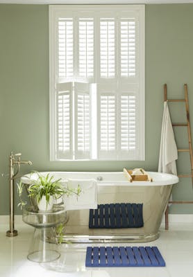 Bathroom painted in grey/ green 'Boringdon Green' with a silver bathtub under a large window.