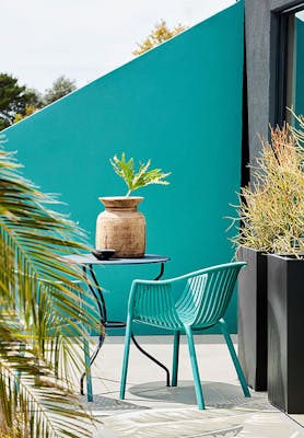 Outside dining area with blue green 'Canton' asymmetrical wall with dining room table and chairs with plants.