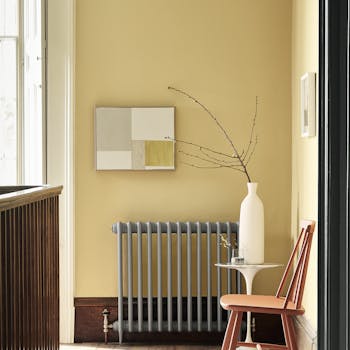 Landing decorated with Light Gold walls, grey radiator, an orange chair, a patterned rug, and a white side table and vase.