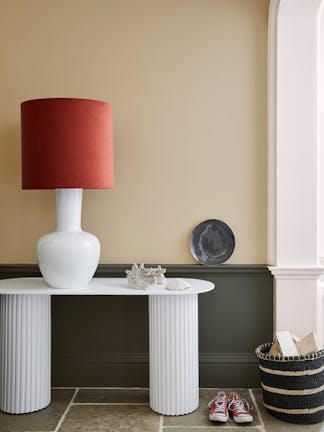 Pale brown neutral hallway (Lute) with lower wall painted in grey green (Pompeian Ash) and a white side table and large lamp.