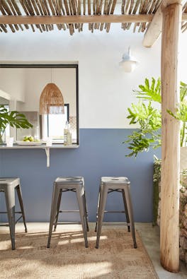 Outdoor breakfast bar with three stools against a wall painted in deep blue (Juniper Ash) and neutral white (Slaked Lime).