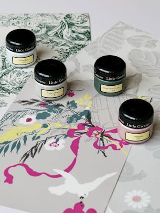 Four Little Greene sample paint pots in French Grey, Wood Ash, Three Farm Green and Hellebore on top of wallpaper samples.