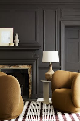 Deep brown paneled living space (Chocolate Colour) with contrasting dark yellow armchairs sat next to a fireplace and lamp.