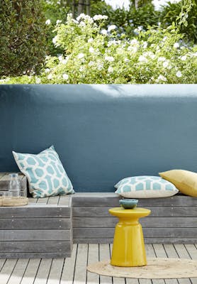 Outside seating area with an Air Force Blue back wall and a wooden panelled bench with cushions.