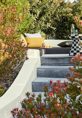 Exterior steps with an off white (White Lead) wall leading up to a lounge area with trees surrounding.