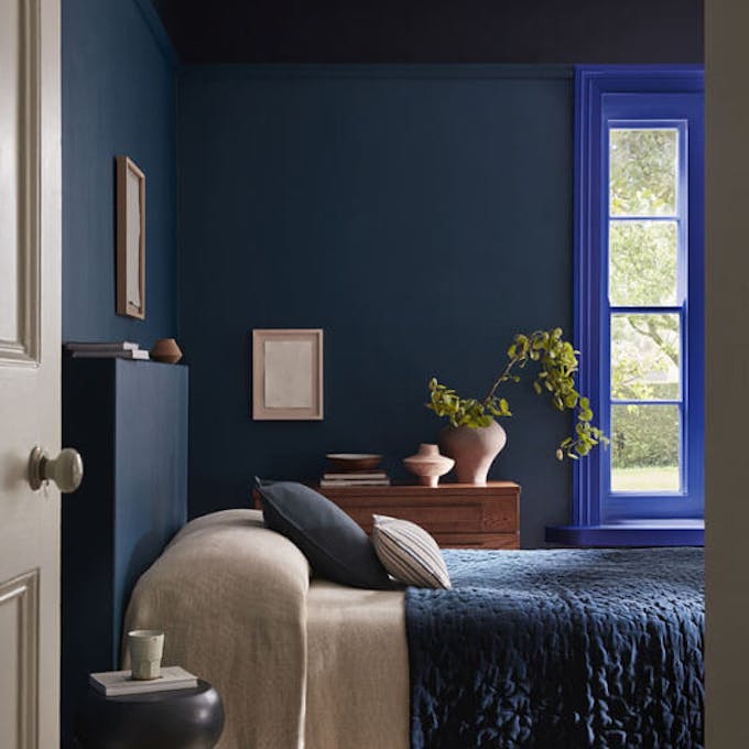 Bedroom painted in rich blue shade 'Royal Navy' with a bright blue 'Smalt' window frame, dark blue on the ceiling and a bed under the window.