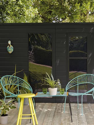 Wooden summer house with Lamp Black walls alongside wooden decking and Turquoise Blue and yellow (Trumpet) garden furniture.