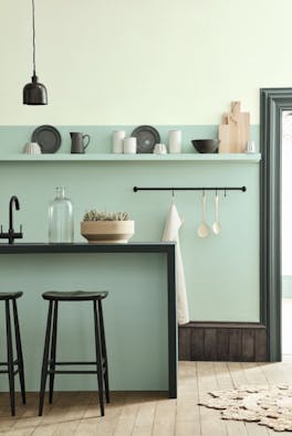 Kitchen space in varying shades of aquamarine with a breakfast bar and stools on a wooden floor.