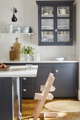 Child's seat placed at a kitchen counter with kitchen units painted in dark blue shade 'Juniper Ash' and the walls in white shade 'Shirting'.