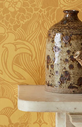 Close-up of yellow floral wallpaper (Dahlia Scroll - Giallo) alongside a light mantlepiece with brown vases on top.