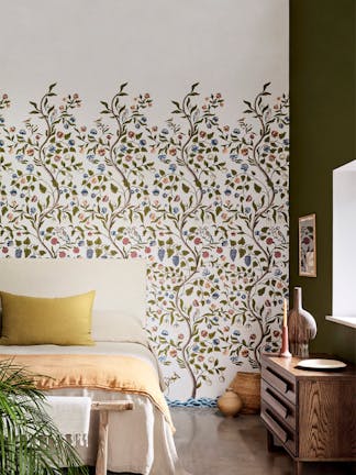 Bedroom with off white floral mural wallpaper (Mandalay - Ceviche) with a bed, sideboard and plant. 