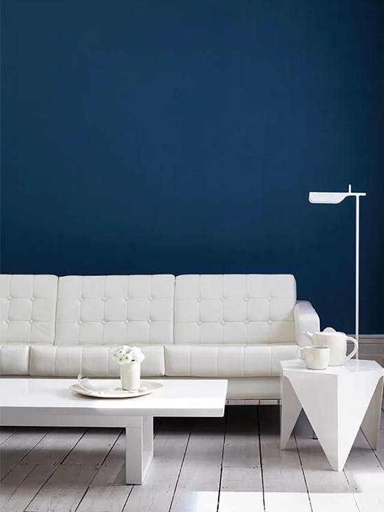 Living room featuring a dark Royal Navy wall with a contrasting sofa, lamp and coffee tables in white on light wood flooring.