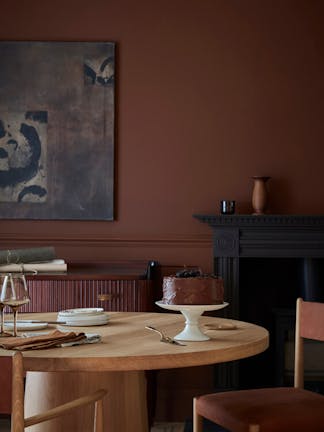 Dining space colour drenched in deep brown shade 'Ganache' with a wooden table and chairs under abstract wall art.