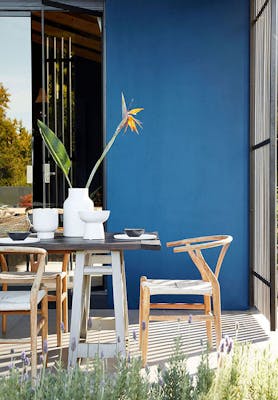 Outdoor breakfast patio space painted in rich blue 'Mazarine' with a wooden dining room table and chairs.