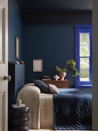 Bedroom painted in rich blue shade 'Royal Navy' with a bright blue 'Smalt' window frame, dark blue on the ceiling and a bed under the window.