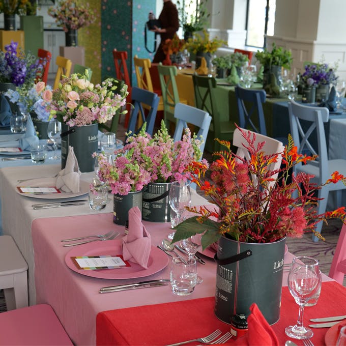 Long tables with Little Greene paint tins holding flowers, along with multi-colored tablecloths, chairs and plates.