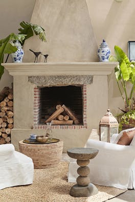 Outdoor living space with two armchairs facing a large log fire with the wall and surround painted in warm neutral shade 'Rolling Fog'.