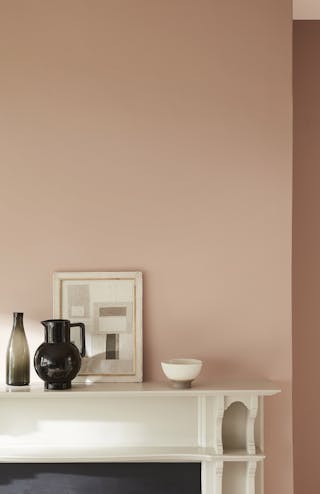 Close-up of artwork leaning on a shelf behind a black jug, in front of a wall painted in a neutral pink, 'Masquerade - Mid'.