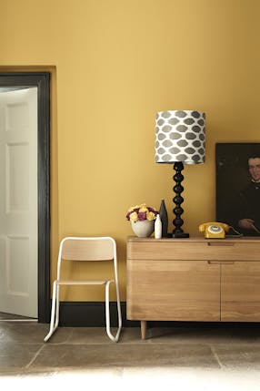 Hallway painted in mustard yellow (Yellow-Pink) with a wooden side table and chair.