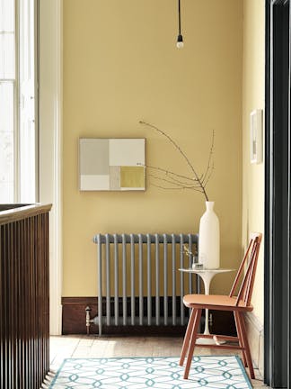 Landing decorated with Light Gold walls, grey radiator, an orange chair, a patterned rug, and a white side table and vase.