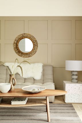 Paneled living space painted in warm neutral 'Travertine' with two sofas and a wooden coffee table.