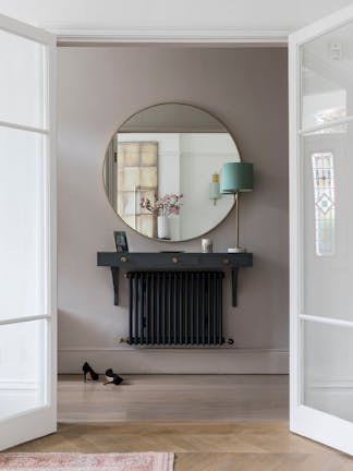 Interior double doors that open into a hallway with grey walls and a round mirror mounted above a side table and radiator.