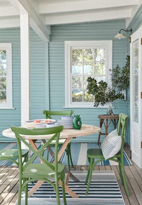 Outside dining area with cladded wall painted in pale blue (Celestial Blue) and a dining room table with green chairs.