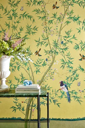 Home study with a bright yellow floral and bird wallpaper (Belton Scenic - Sunbeam) with a desk and vase placed in front.