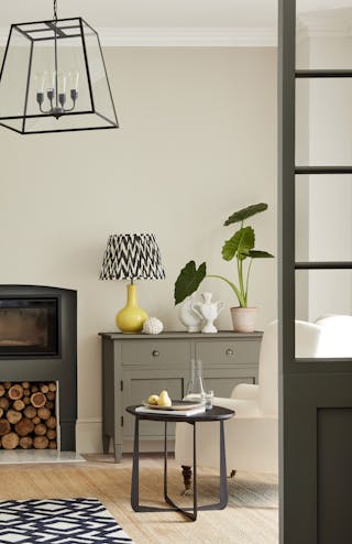 Neutral living space painted in 'Portland Stone' with grey drawers, plants and a patterned lamp in yellow, grey and white.