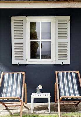 Two deck chairs in front of an exterior window with light grey shutters and a wall painted in deep black blue 'Basalt'.