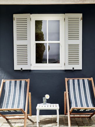 Two deck chairs in front of an exterior window with light grey shutters and a wall painted in deep black blue 'Basalt'.