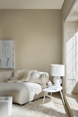 Living room in 3 different neutral shades (Silent White) with a sofa, table and lamp next to a window.