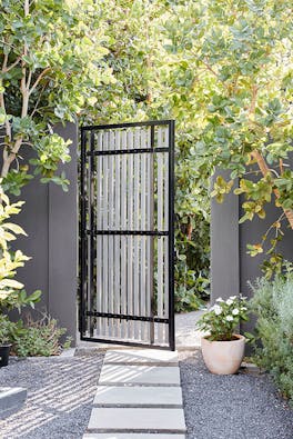 Garden gate with stepping stones and walls painted in grey shade 'Arquerite' with trees surrounding.