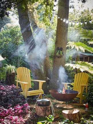 Forest with two bright yellow garden chairs (Giallo) with a barbeque lit surrounded by trees.