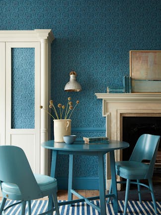 Dining space with a tonal blue wallpaper (Hoja - Air Force Blue) and white (Shirting) cupboard with blue table and chairs.