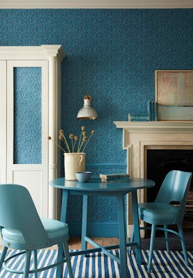 Dining space with a tonal blue wallpaper (Hoja - Air Force Blue) and white (Shirting) cupboard with blue table and chairs.