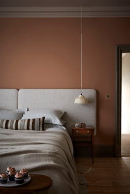 Bedroom painted in muted pink shade 'Split Pink' with a double bed next to a wooden sidetable.