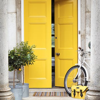 Front door painted in bright yellow 'Mister David' with two trees and a bike under pillars.